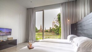 A hotel room with a large bed, a TV, and a view of a temple through the window. - Sala Ayutthaya (Ayutthaya)