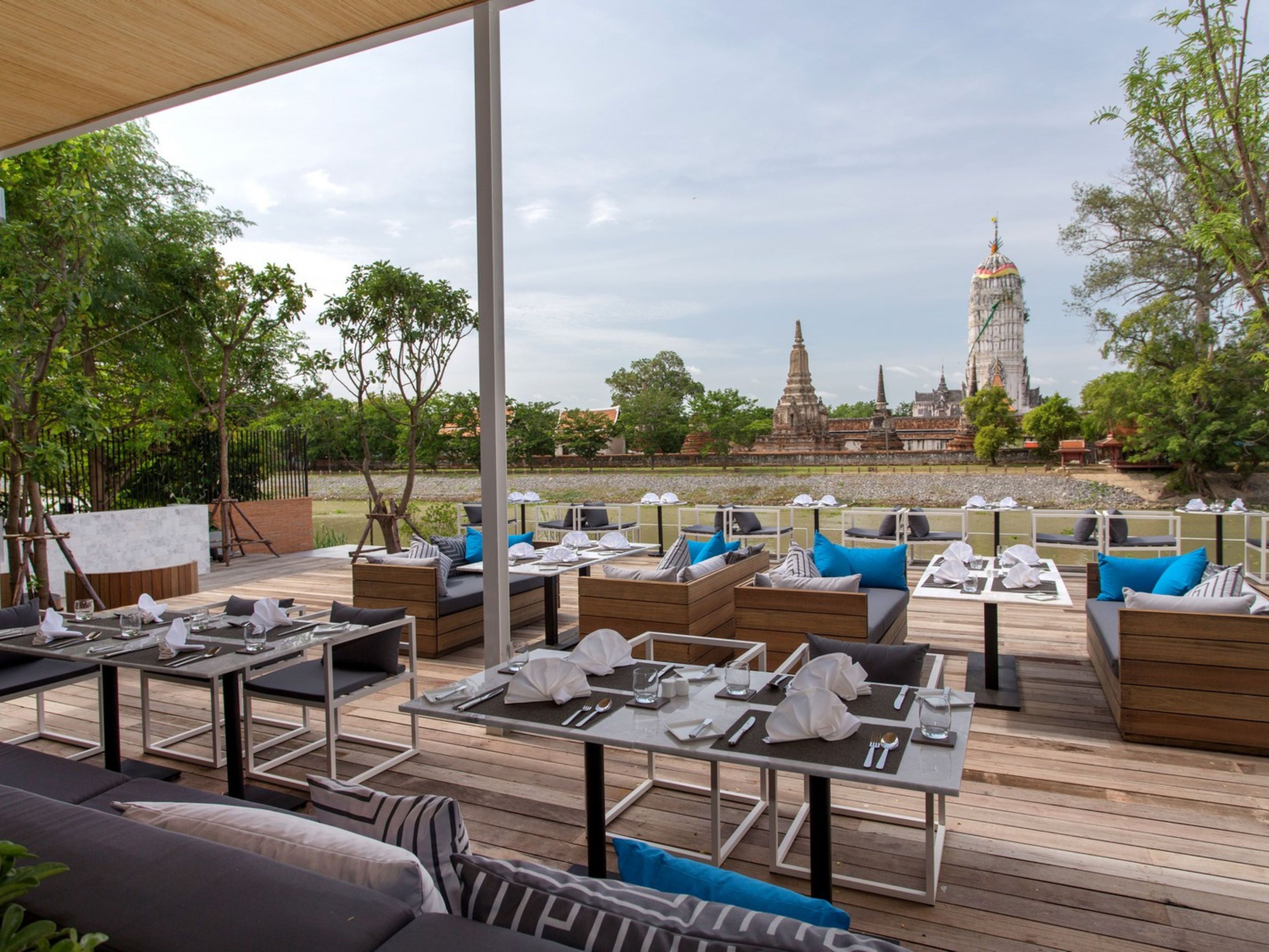 Un área de comedor al aire libre con mesas y sillas, una terraza de madera y vistas a templos antiguos al fondo.