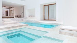 Una piscina interior moderna con agua azul cristalina, rodeada de paredes blancas y escalones de mármol.