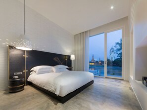 A modern hotel room with a large bed, a nightstand, a lamp, and a view of a temple through the window. - Sala Ayutthaya (Ayutthaya)