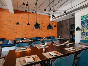 A restaurant interior with brick walls, blue seating, and pendant lighting.