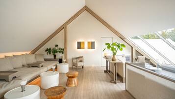 Quarto moderno estilo loft, com teto inclinado, sofá, mesinhas de madeira e um vaso de planta.