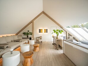 A modern loft-style room with a sloped ceiling, a sofa set, wooden side tables, and a potted plant. - Sala Ayutthaya (Ayutthaya)