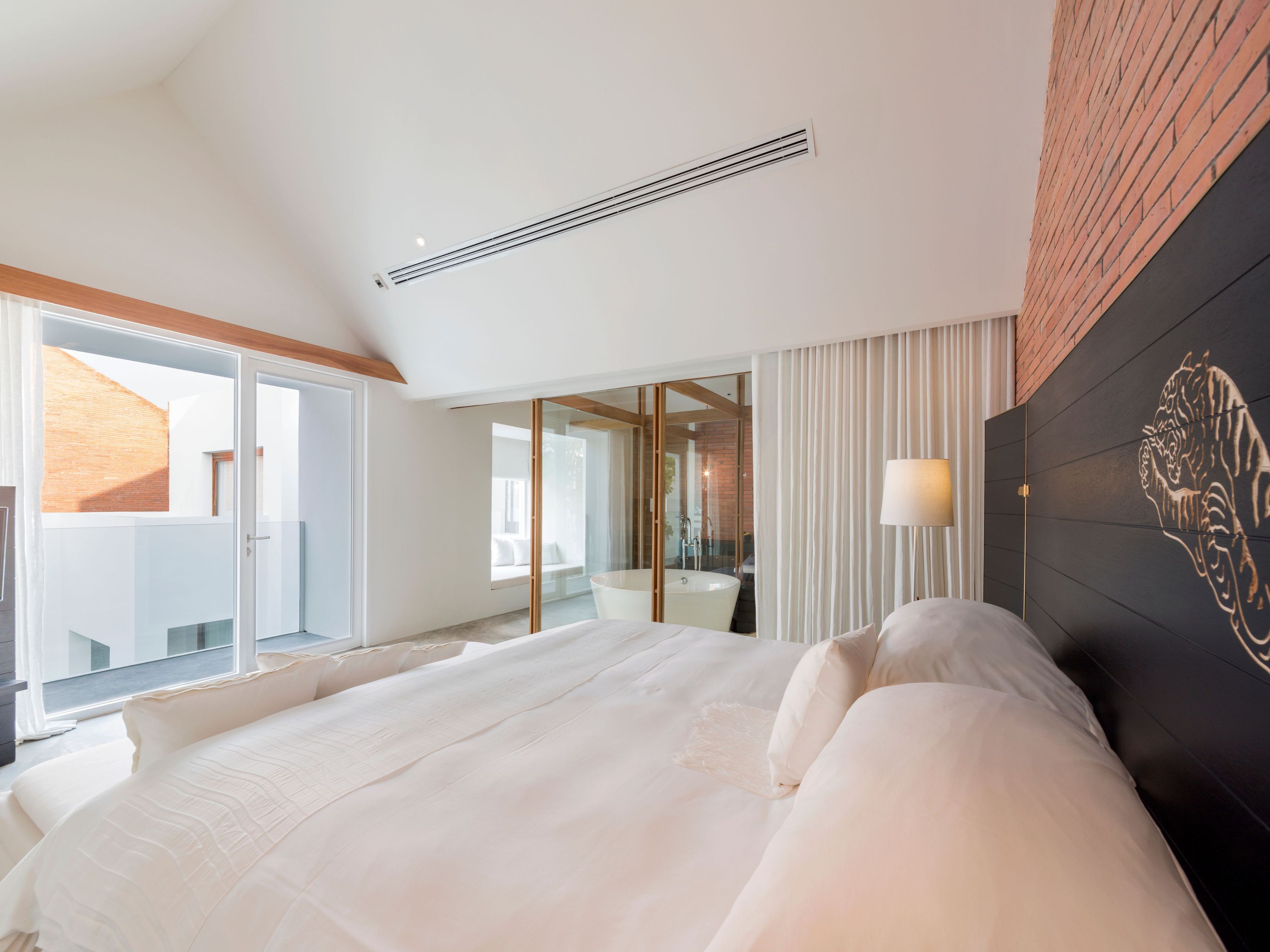 A modern hotel room with a large bed, a bathroom with a bathtub, and a view of the outside.