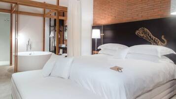 A modern bedroom with a large bed, a wooden headboard, a brick accent wall, and a white bathroom with a bathtub.