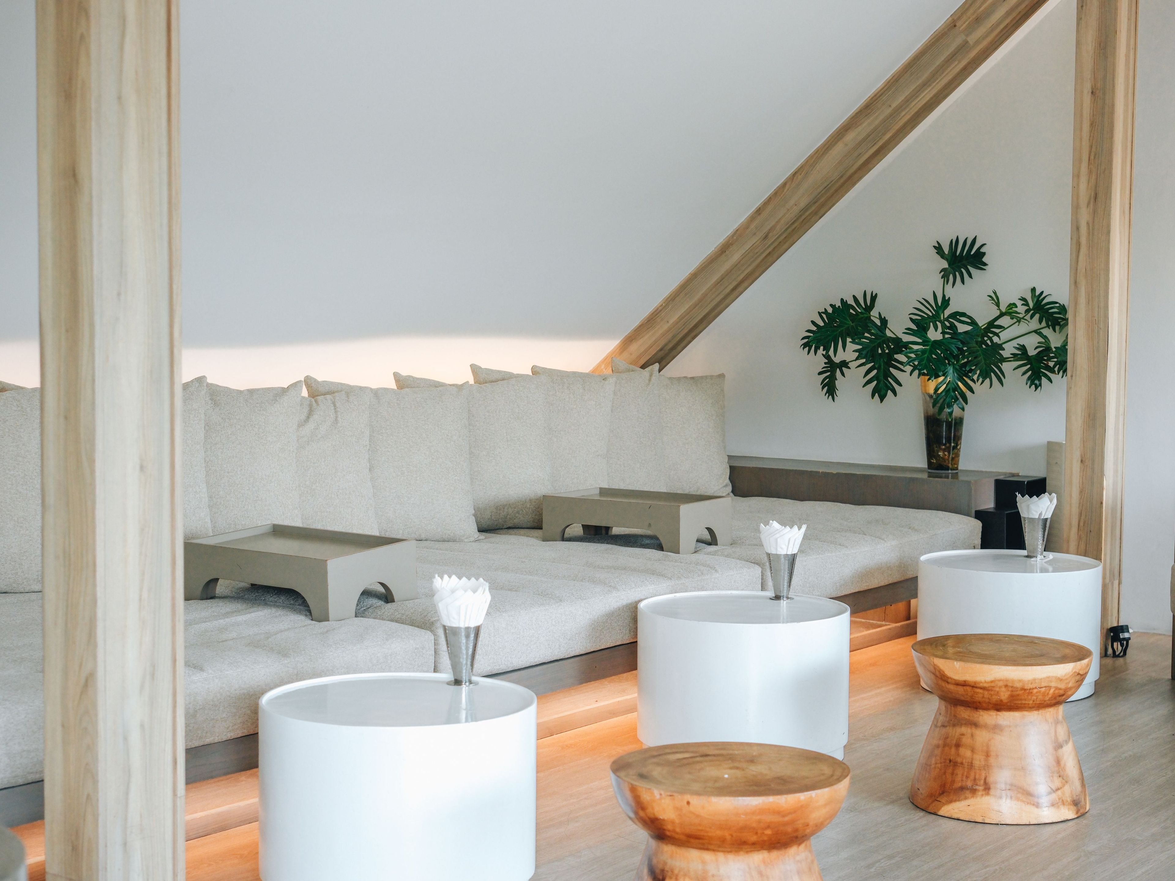 Een moderne, minimalistische kamer met een schuine kap, een bank met kussens, en drie houten krukken met witte poten.