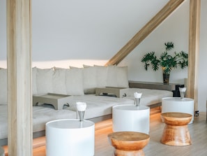 A modern, minimalist room with a sloped ceiling, a sofa with cushions, and three wooden stools with white bases.