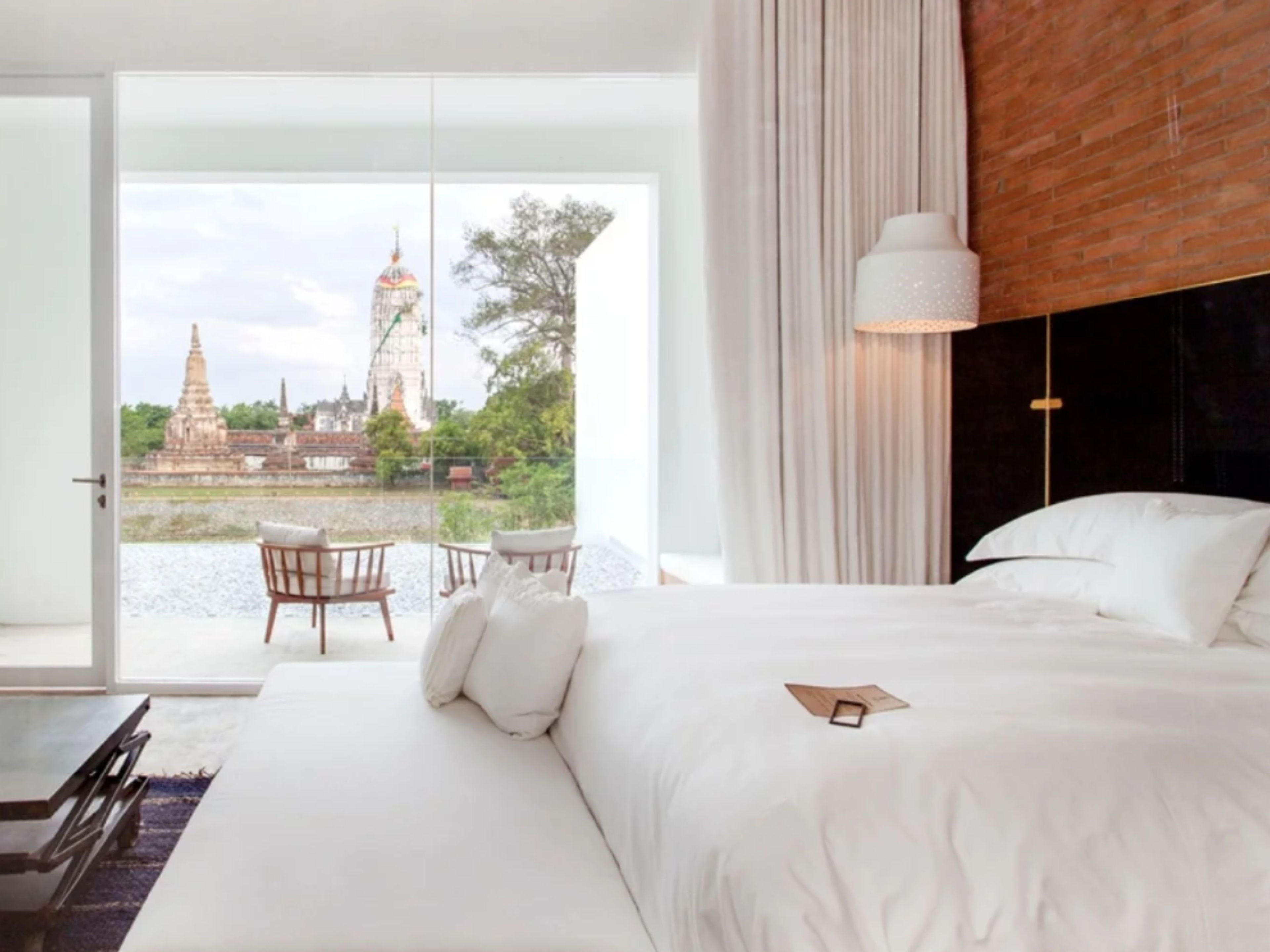 A bedroom with a large bed, a view of a temple through a glass door, a table with chairs, and a hanging light fixture.