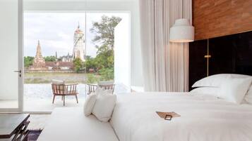 Un dormitorio con una cama grande, vistas a un templo a través de un ventanal, una mesa con sillas y una lámpara colgante.