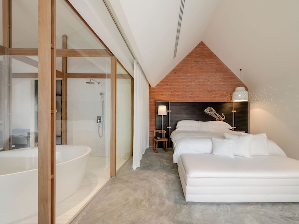 Un dormitorio moderno con una cama grande, un área de ducha separada y un baño a la vista.