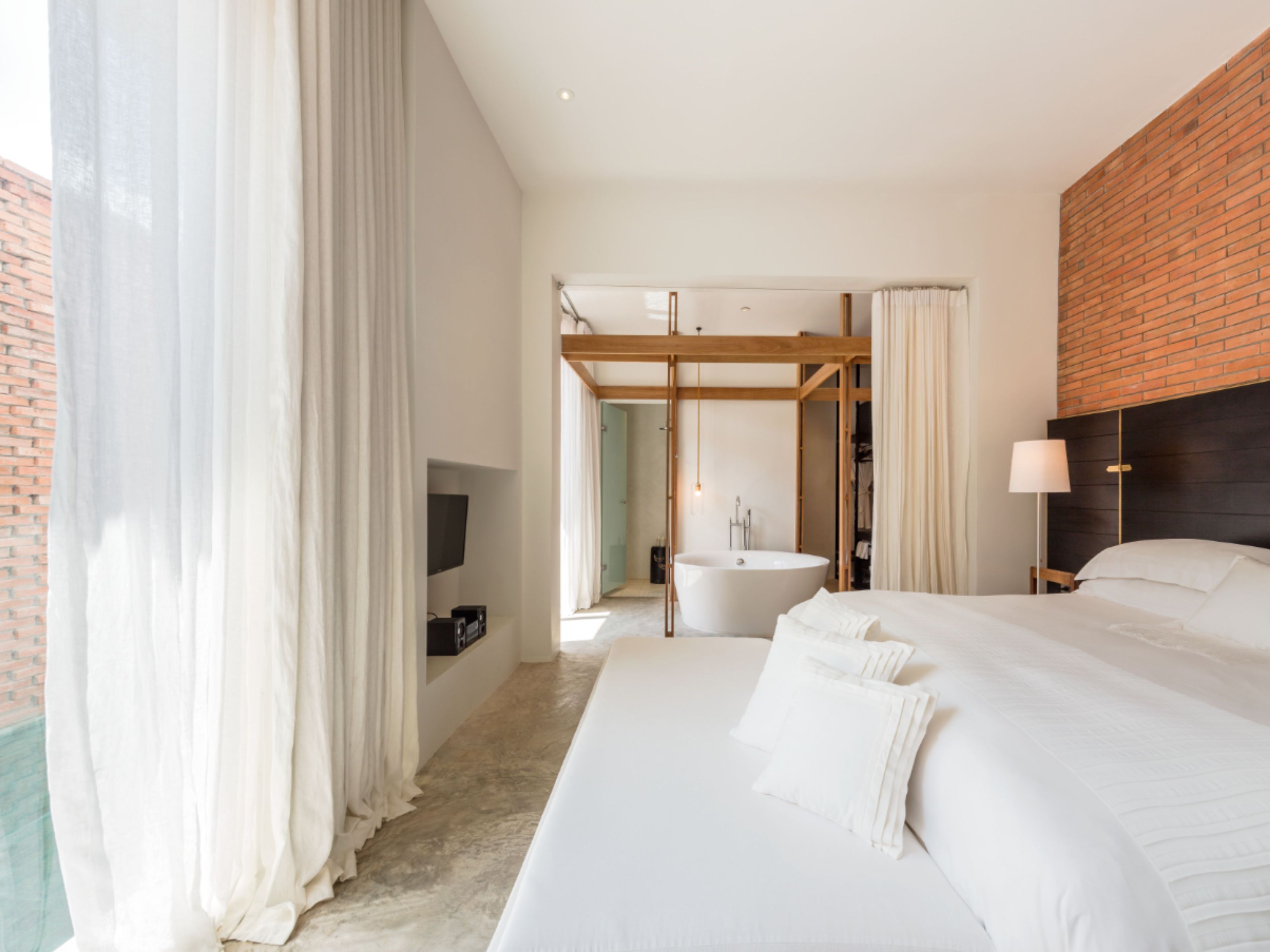 Ein modernes Hotelzimmer mit einem großen Bett, einem Flachbildfernseher, einer Badewanne und einer Holzbalkendecke.