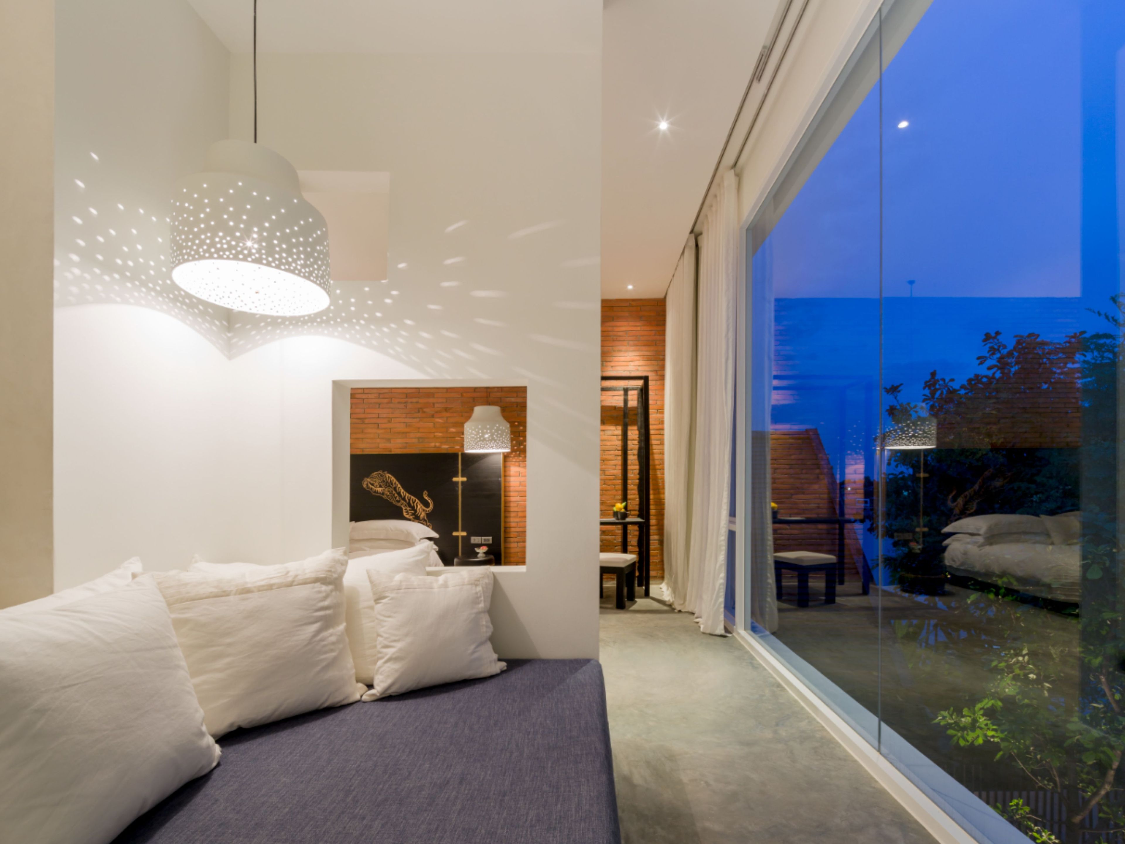 Een moderne slaapkamer met een groot raam, een bed met witte beddengoed en een wandlamp.