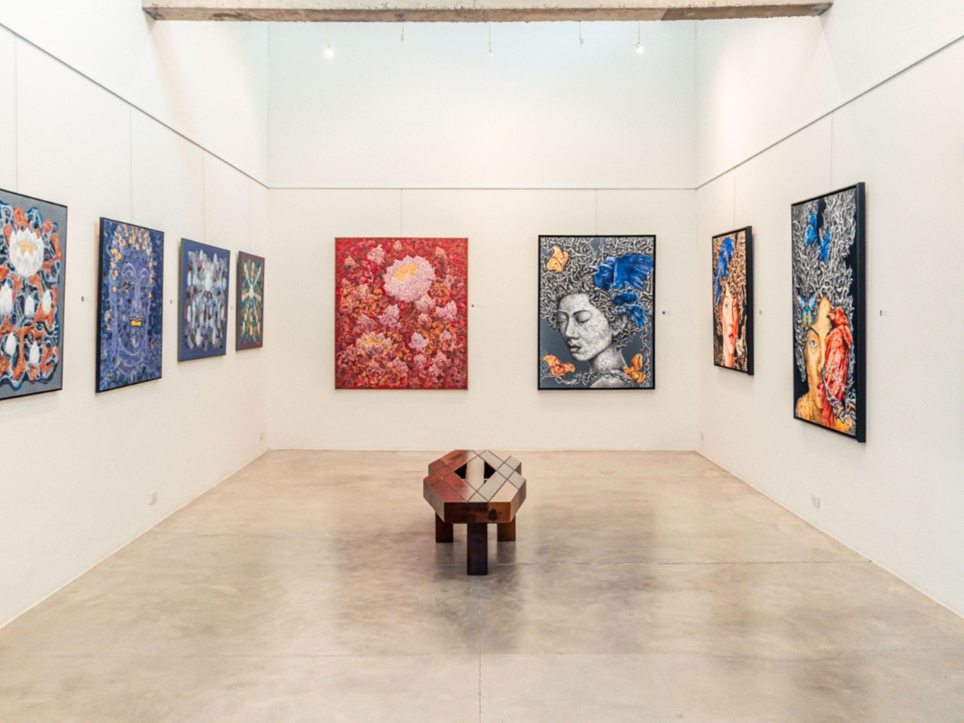 An art gallery with paintings on the walls and a wooden bench in the center.