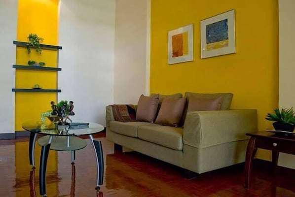 Un salon avec un canapé, une table basse en verre et un mur d’accent jaune.