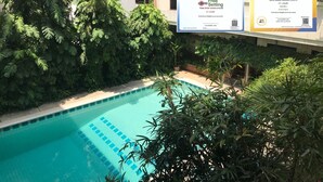 An outdoor swimming pool surrounded by lush greenery, with two informational signs about COVID-19 safety measures. - PT Court (Bangkok)