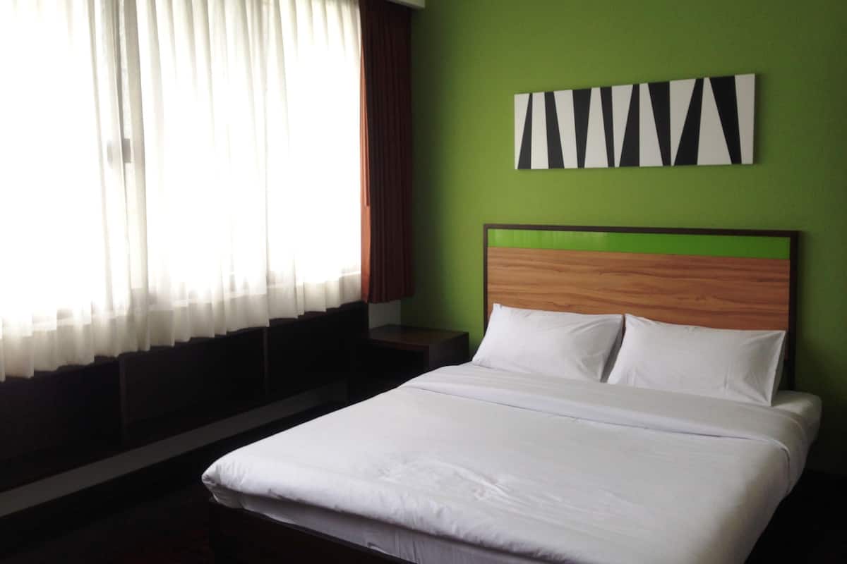 Habitación de hotel con cama, mesita de noche, ventana con cortinas y pared verde decorada con un cuadro blanco y negro.