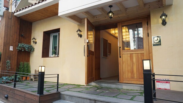 L’entrée d’un hôtel, avec une façade en bois, une porte en verre et une petite fenêtre ornée de plantes.