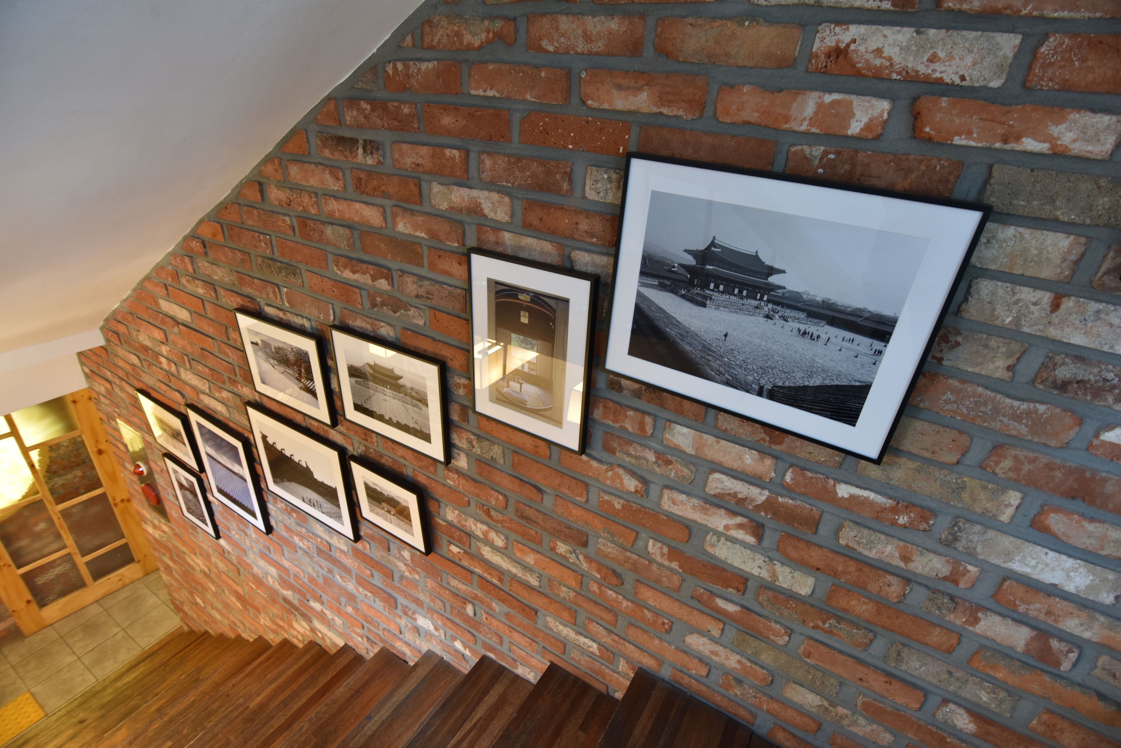 A brick wall with framed pictures and a black and white photo.