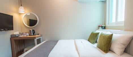 A hotel room with a bed, a desk with a computer, a TV, a mirror, an air conditioner, and a window with a view.