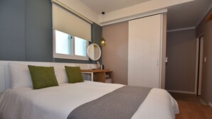 Un lit bien fait, avec une couette blanche et deux oreillers verts, une table de chevet avec une lampe et un miroir au-dessus.