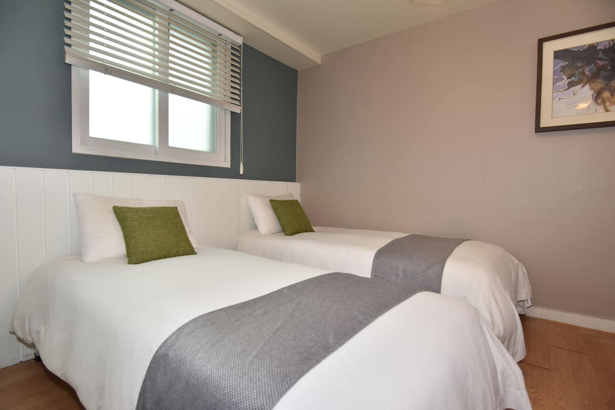 Une chambre avec deux lits, du linge de lit blanc, des oreillers verts et un plaid gris.