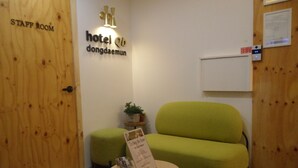 Un hall d’hôtel avec un canapé vert, une petite table sur laquelle est posée une pancarte, et une porte en bois portant l’inscription « SALLE DU PERSONNEL ».
