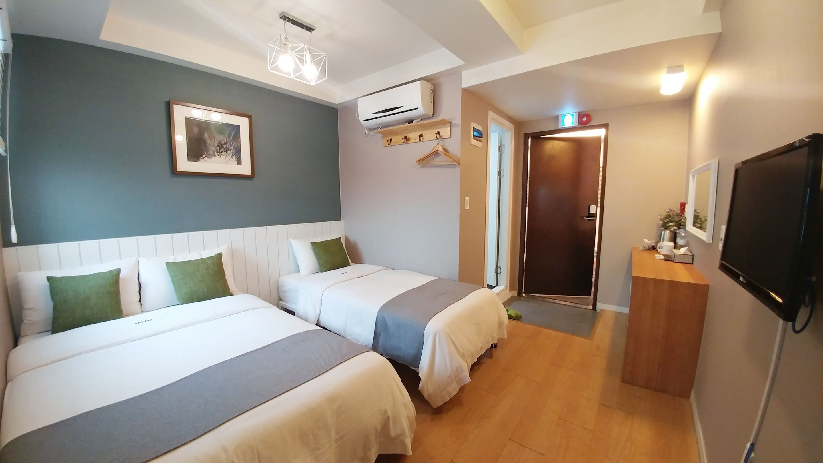 A hotel room with two beds, a mounted TV, an air conditioning unit, and a framed picture on the wall.