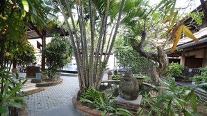 Un patio con una estatua de Buda de piedra, un camino empedrado y diversas plantas tropicales.