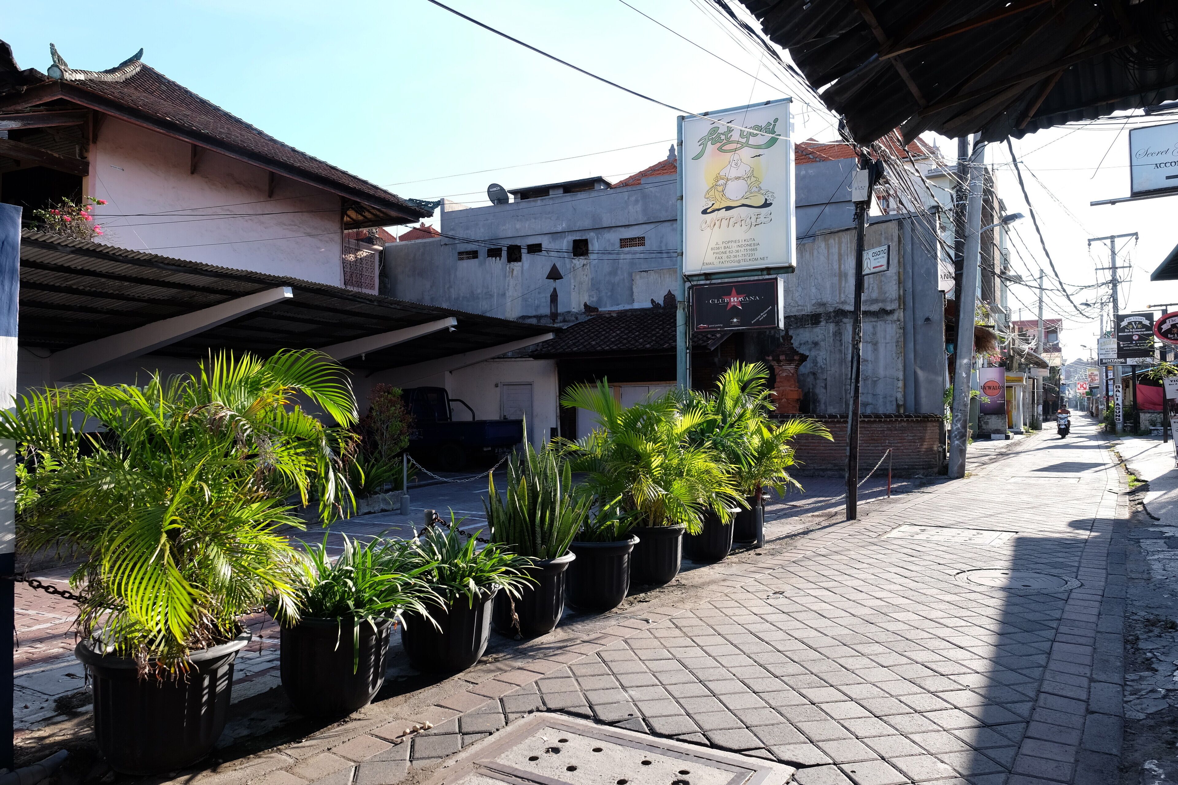 A street with potted plants, a sign for 'Cottages', and a building with a tiled roof.