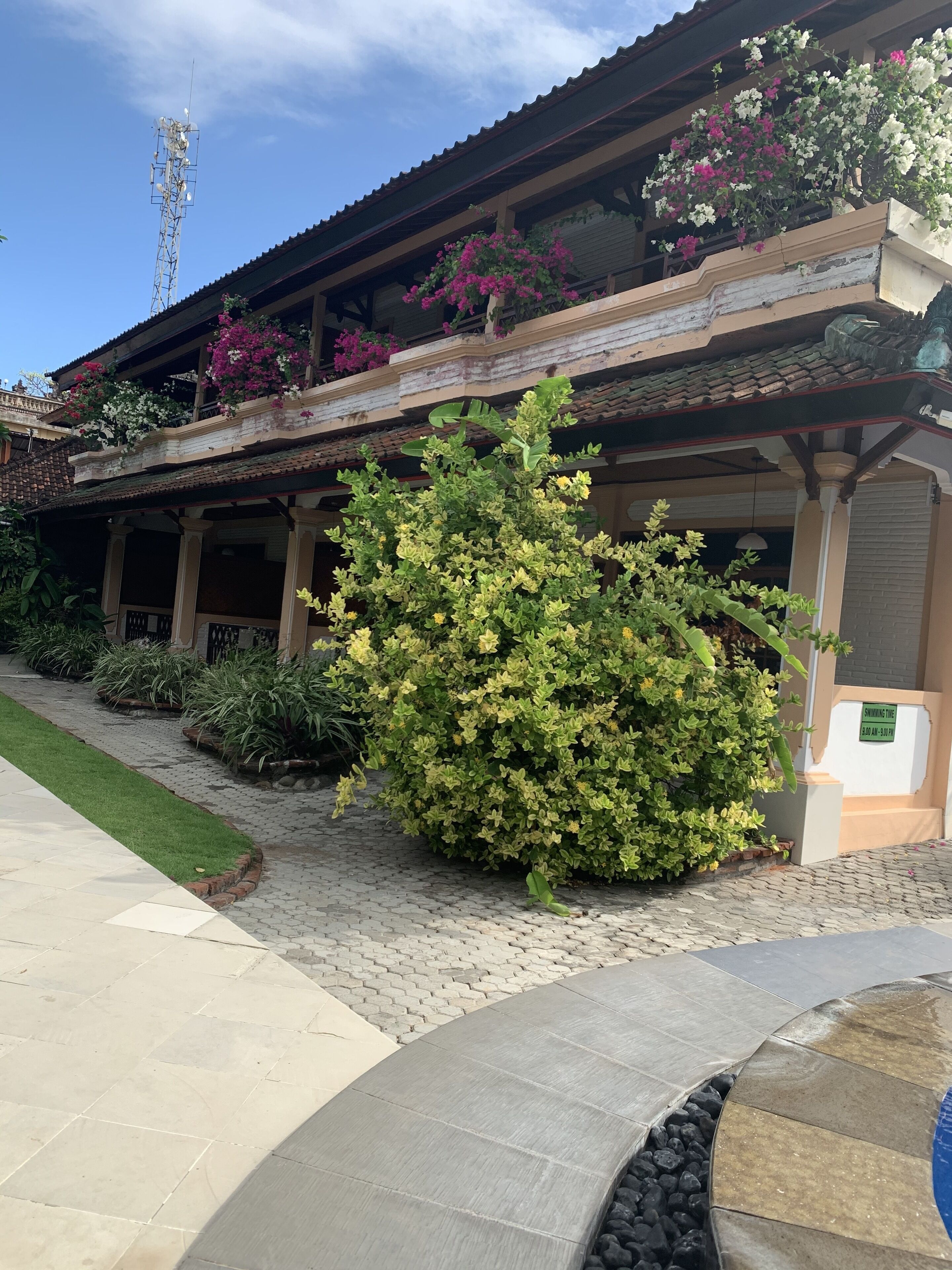 Un edificio con un espacio exterior techado, un pequeño jardín y un letrero que indica una zona para fumadores.
