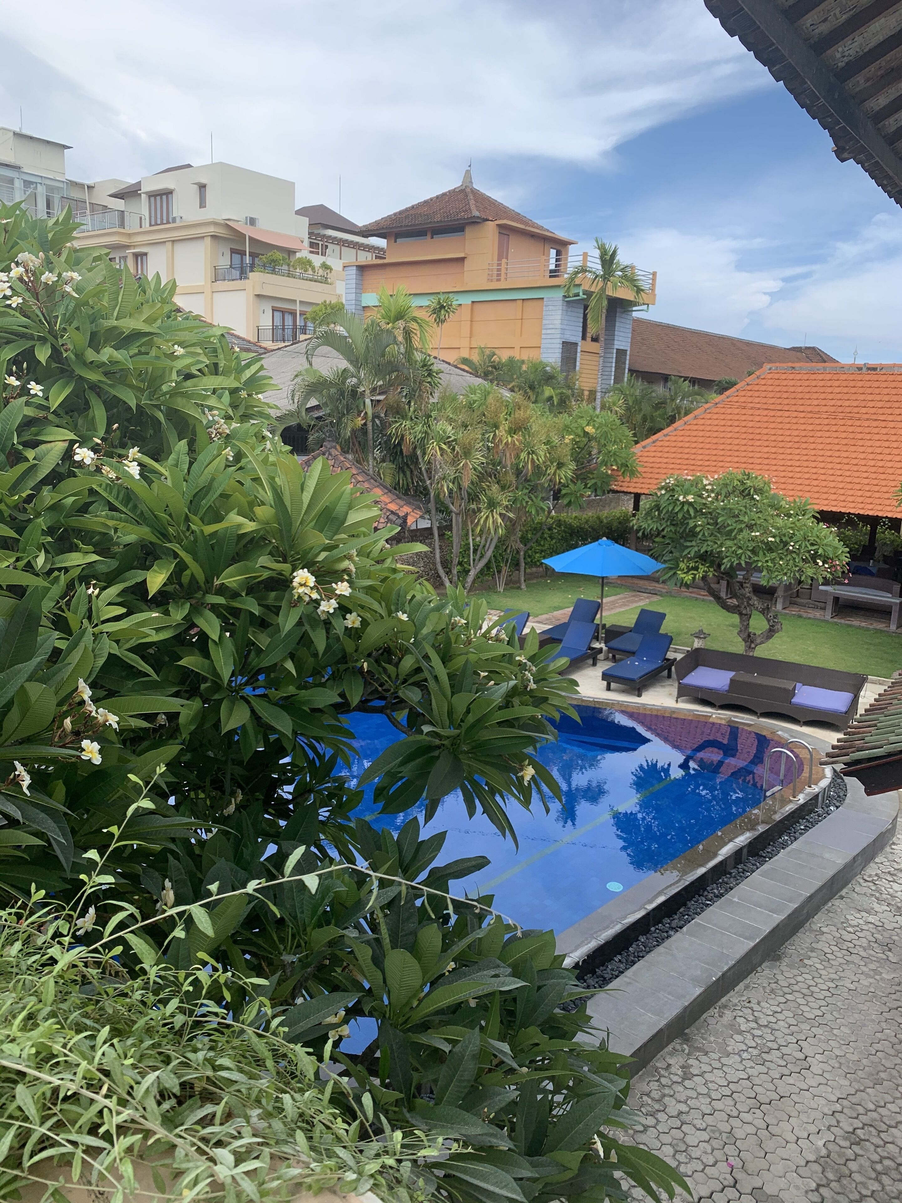 A swimming pool with lounge chairs and umbrellas, surrounded by greenery and residential buildings.