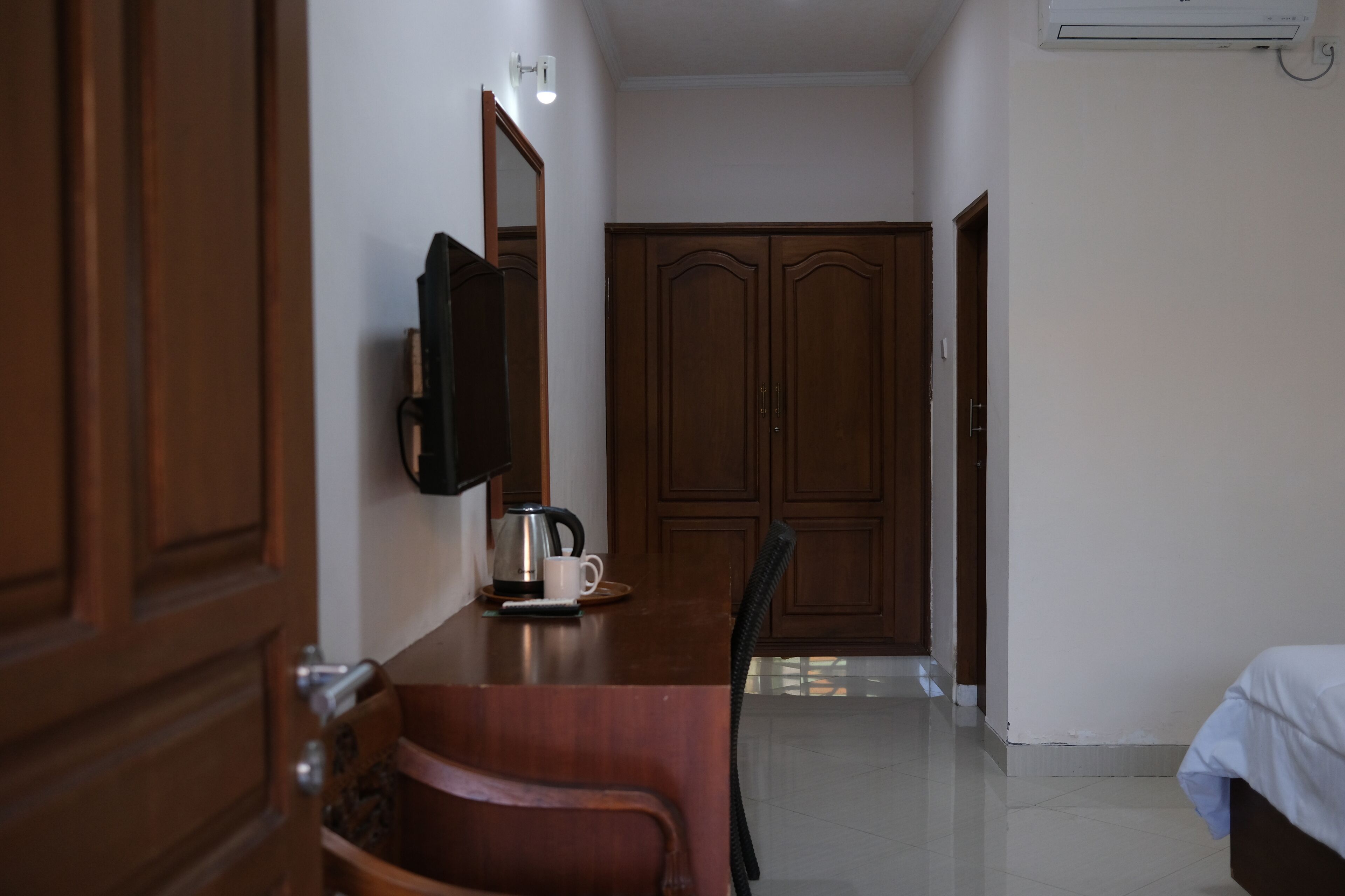 A hotel room with a wooden desk, a chair, a bed, a wardrobe, and a mirror.