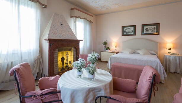 A hotel room with a fireplace, two beds, a round table with vases, and a chandelier. - Villa Revedin (Gorgo al Monticano)