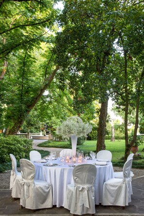 An outdoor dining setup with white tablecloths and chairs, surrounded by lush greenery and trees. - Villa Revedin (Gorgo al Monticano)