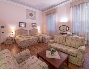 A hotel room with two beds, a sofa, a coffee table, a mirror, and a dining table with a vase of flowers. - Villa Revedin (Gorgo al Monticano)