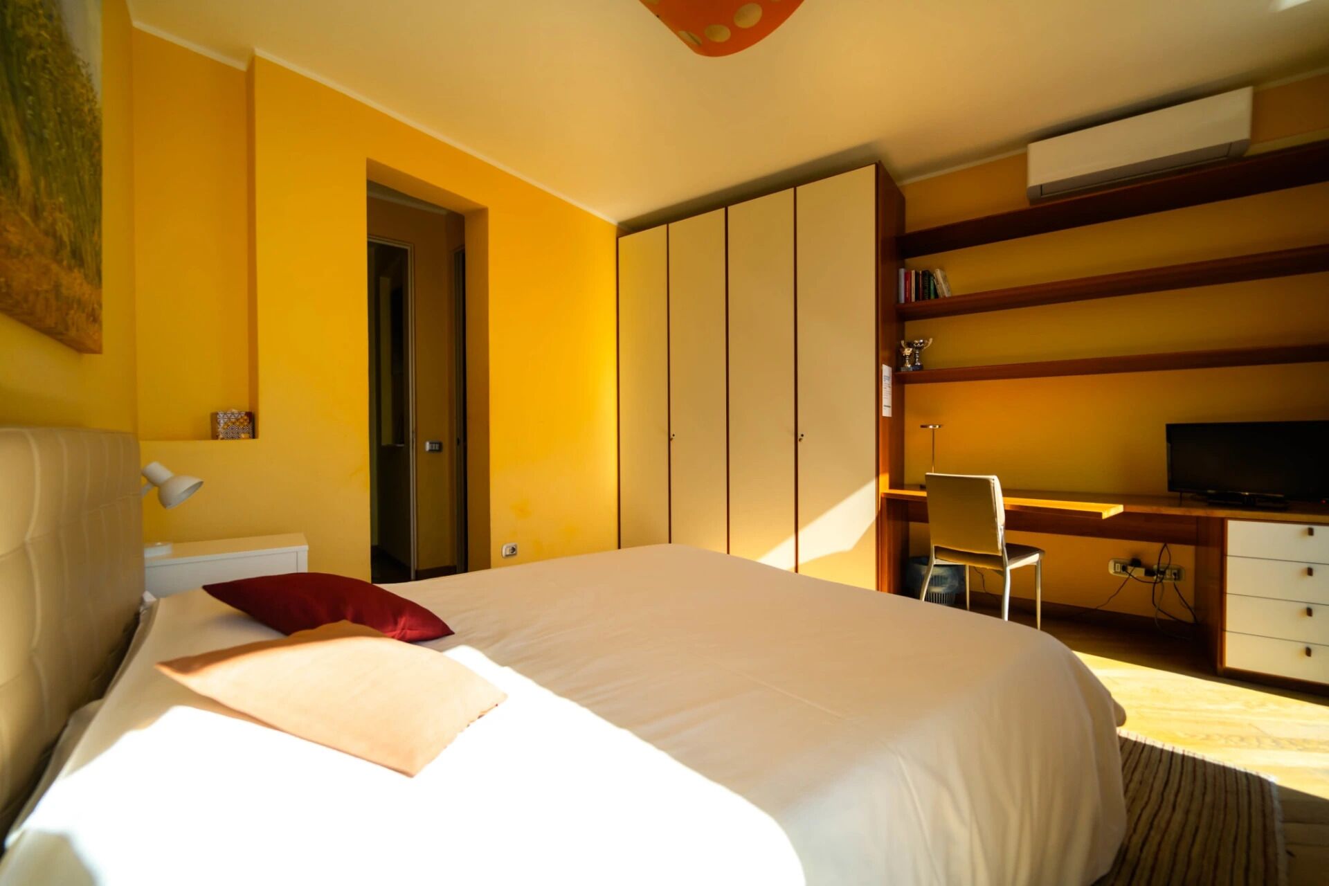 A hotel room with a large bed, a desk with a chair, a television, and a wardrobe.