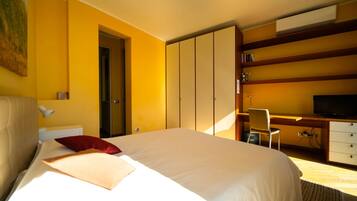 A hotel room with a large bed, a desk with a chair, a television, and a wardrobe.