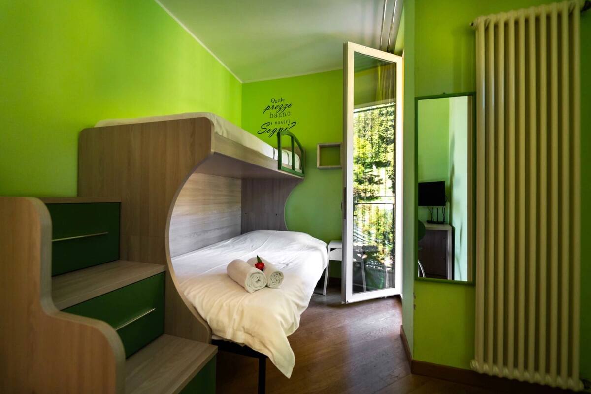 A room with a bunk bed, a desk, a chair, a mirror, and a window with a view of trees.