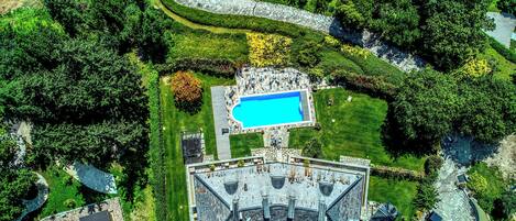 An aerial view of a property with a swimming pool, a covered patio, and a stone building.