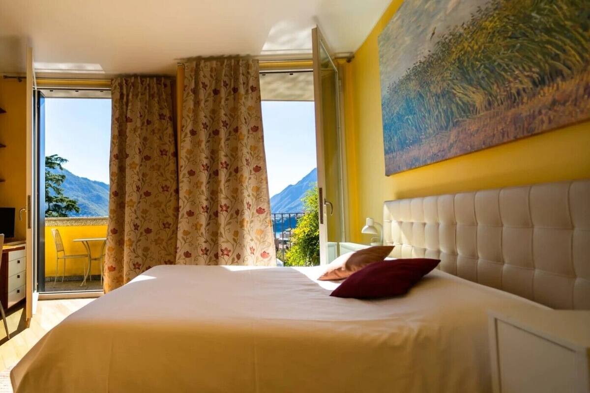 A hotel room with a bed, a painting, and a view of mountains.