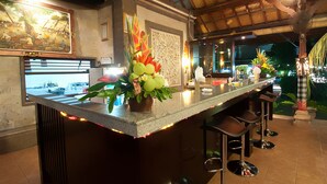 A bar area with a counter, stools, and decorative plants. - Kusnadi Hotel (Legian)