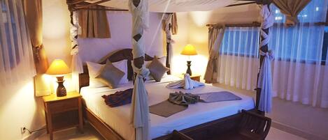 A four-poster canopy bed with pillows, a bedside lamp, and a wooden chair.