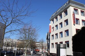 A hotel with a modern facade, multiple windows, and a prominent red sign indicating its name. - Apartment Hotel am Sand (Hamburg)