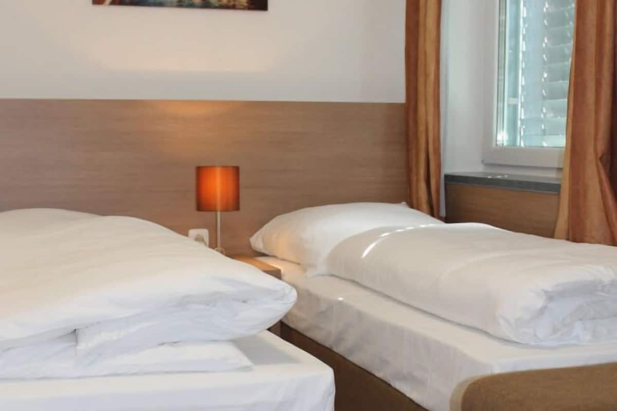 Une chambre d’hôtel avec deux lits, une table de chevet avec une lampe et une fenêtre avec des rideaux.