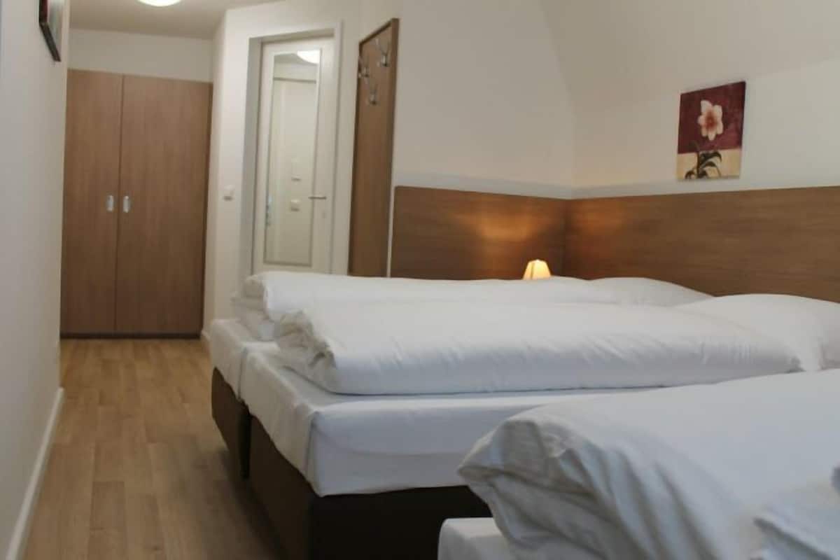 Une chambre avec deux lits, une armoire en bois, une porte et un tableau accroché au mur.