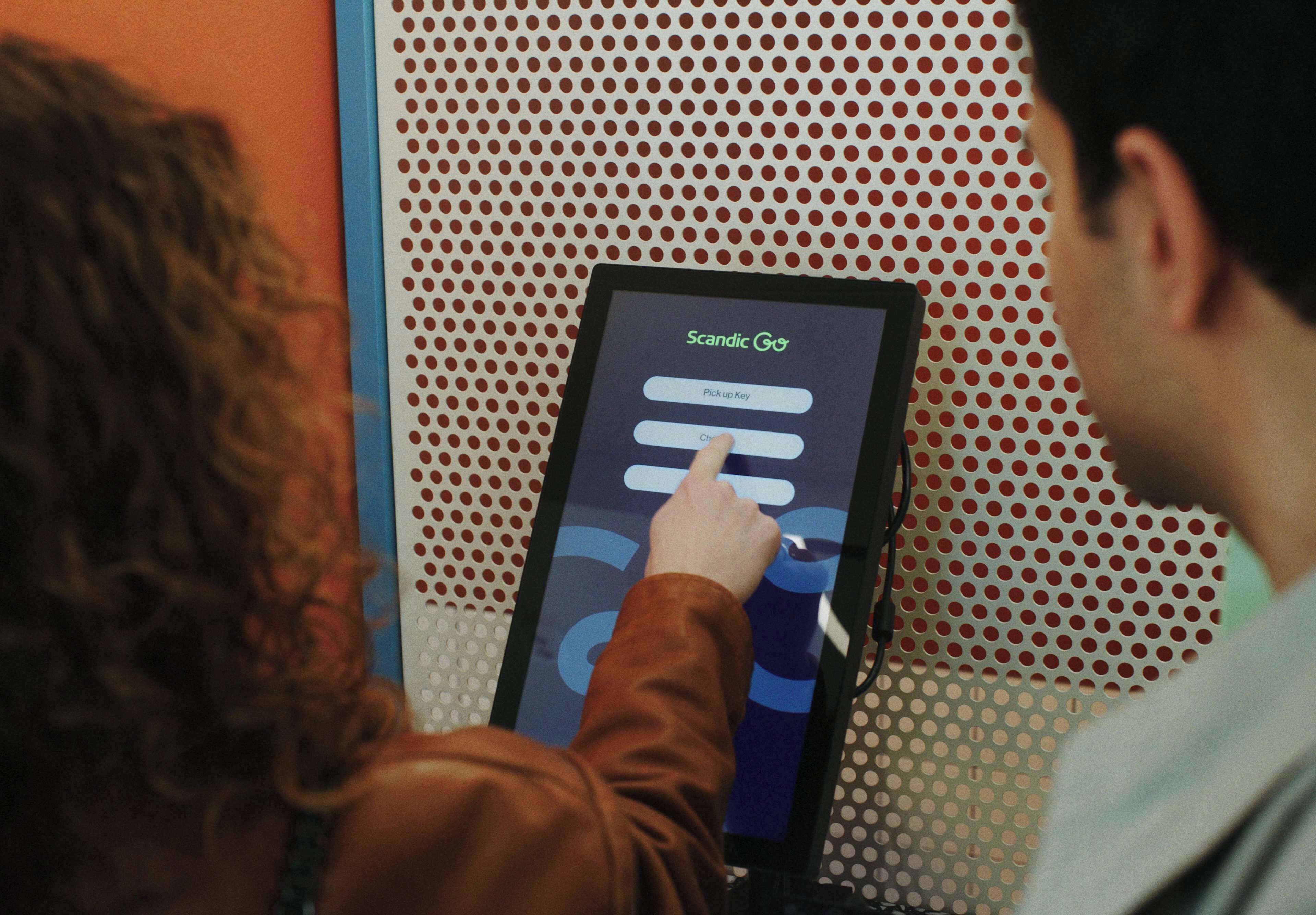 A person interacting with a touchscreen kiosk displaying the text "Scadic Go".