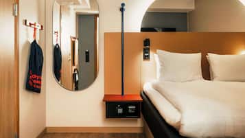 Quarto de hotel com uma cama, um espelho, um porta-casacos e um painel de controlo fixado na parede.
