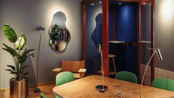A conference room with a wooden table, green chairs, a potted plant, a mirror, and a 'CHAT BOX' sign.