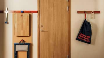 Un armario de madera con una puerta, una silla azul, una tabla de cortar de madera y un bolso negro con texto.