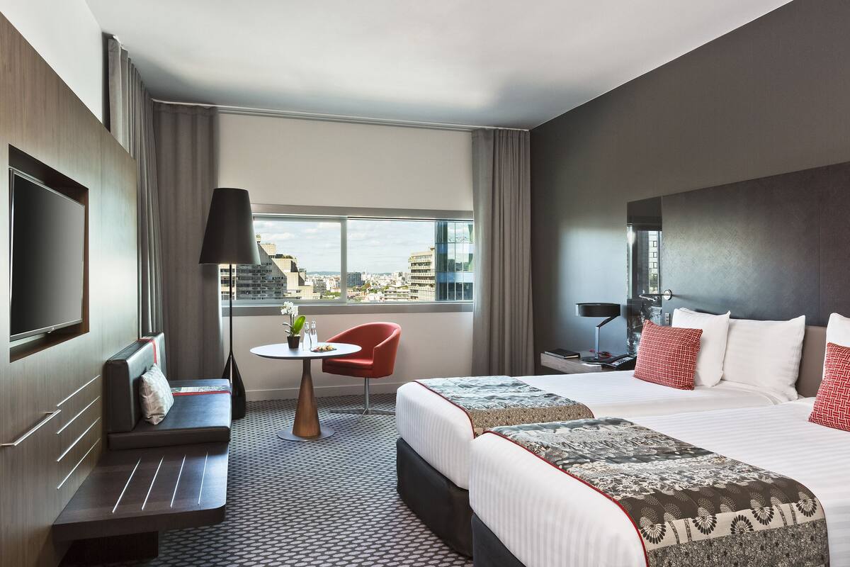 A modern hotel room with a large bed, a sofa, a small table with a lamp, and a TV.
